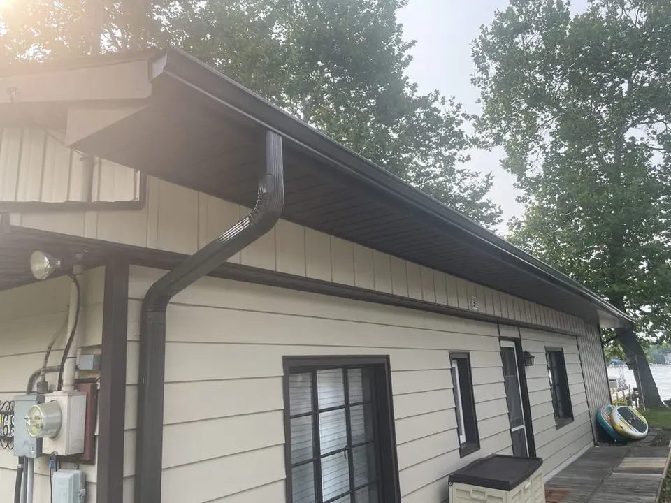 Dark bronze seamless gutter and downspout along the eave of a lakeside home