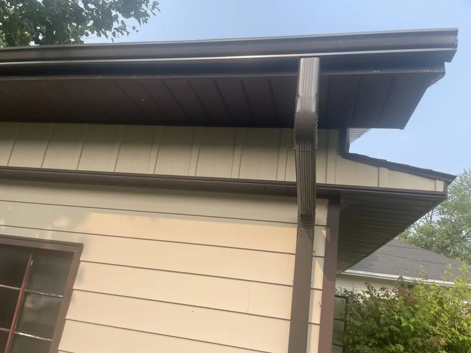 Brown downspout bending under a soffit to run down the wall