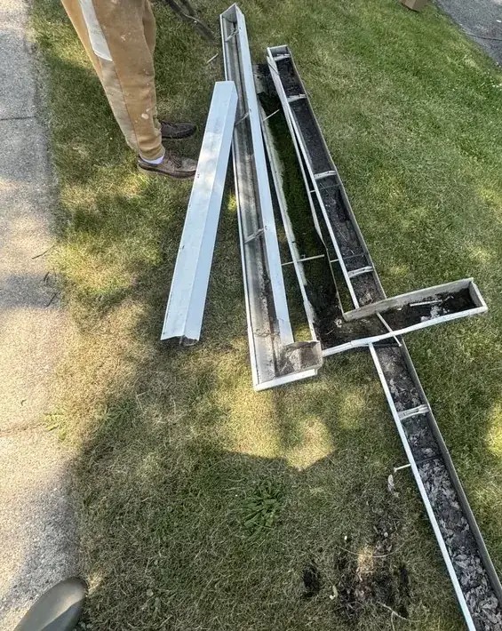 Old gutter sections full of debris laid on a lawn during replacement