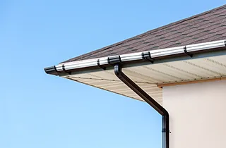 Corner of a house with a white gutter along the eave and a brown downspout dropping from the outlet